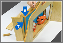 Notranji okvir (6) pomaknite k zadnji steni in vmes vstavite eno ali več slik (7) za ozadja lutkovne predstave. Ozadja nato menjate kot slike pri kamišibaju.